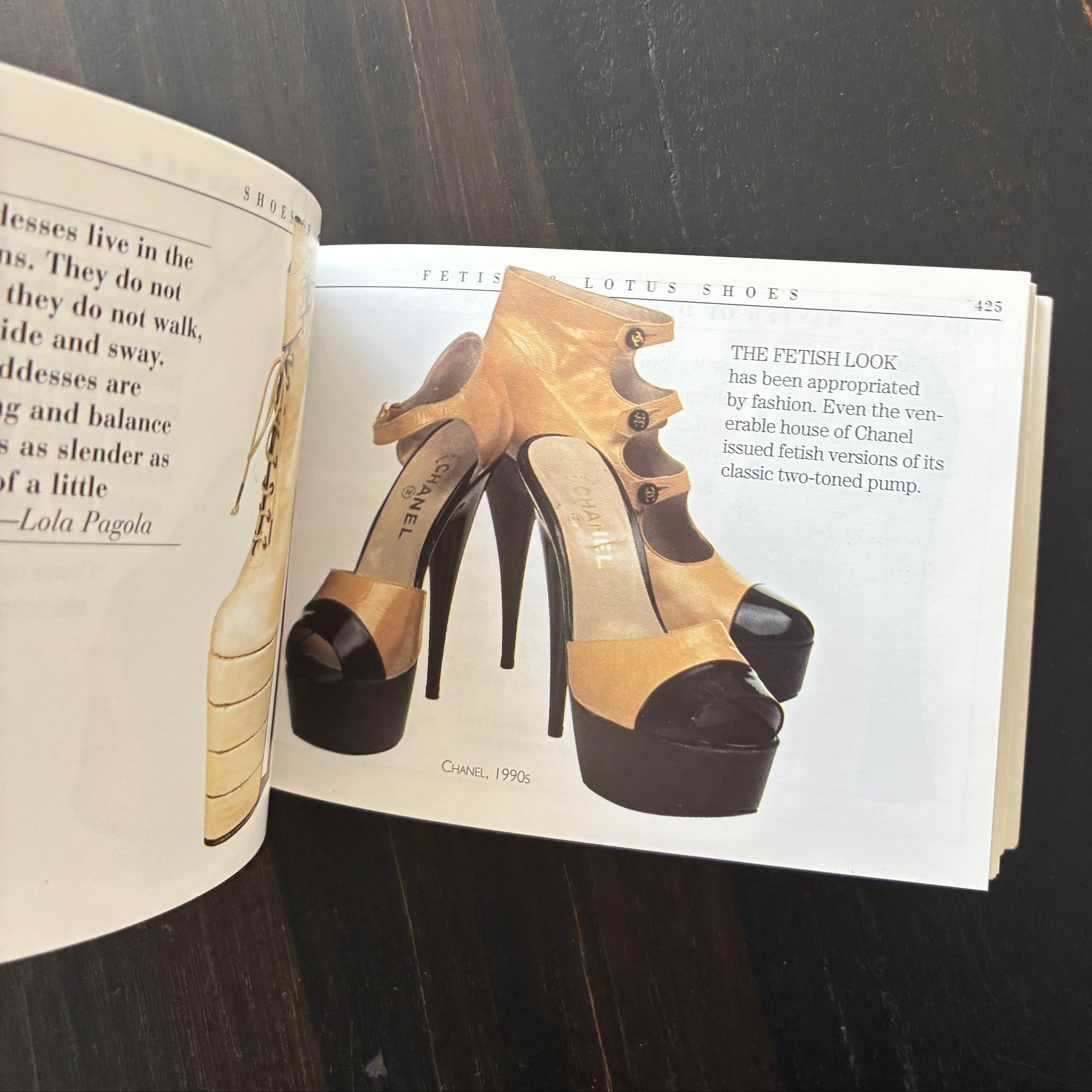 A pair of high-heeled mule shoes in beige and black, shown printed on an open magazine or book page resting on a dark wooden surface.